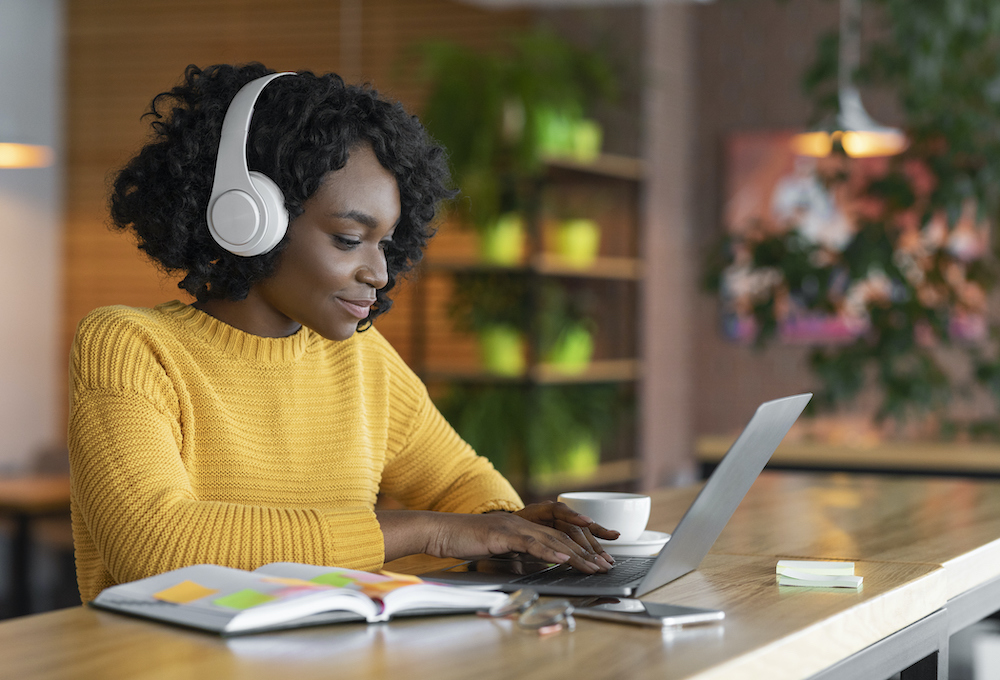 Young woman sitting at laptop with headphones on, learning online