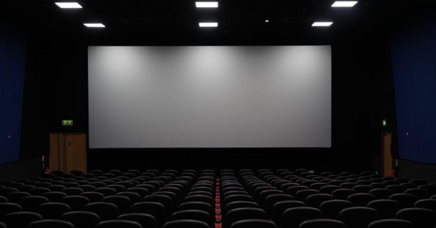 Photo of a movie theater with more than a dozen rows of seats and a large blank screen against the wall.